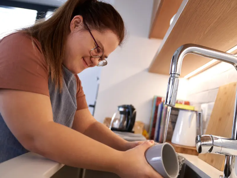 Disabled girl with down syndrome doing the dishes at home