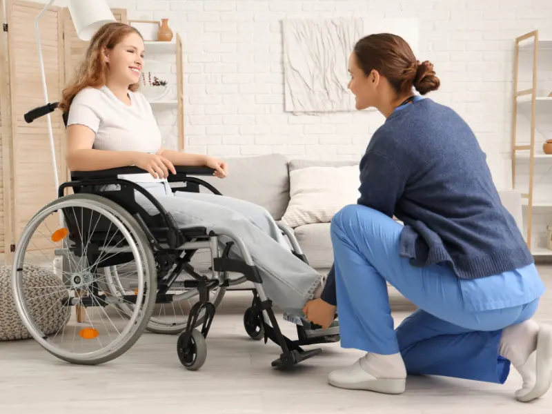 Disabled woman in wheelchair smiling at nurse in living room