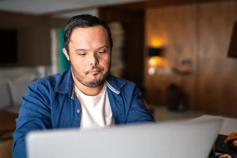 Disabled man with down syndrome sitting at desk using laptop