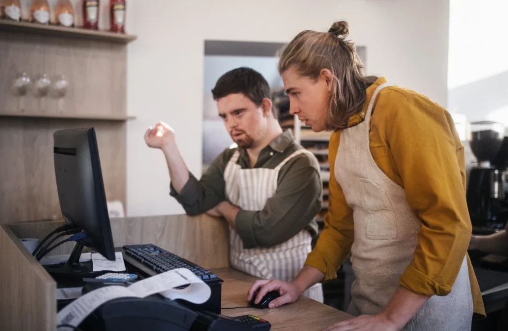 Disabled man with down syndrome working with colleague at cafe