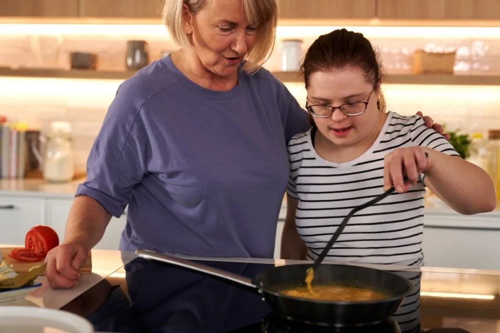Support worker cooking with disabled girl with down syndrome in kitchen