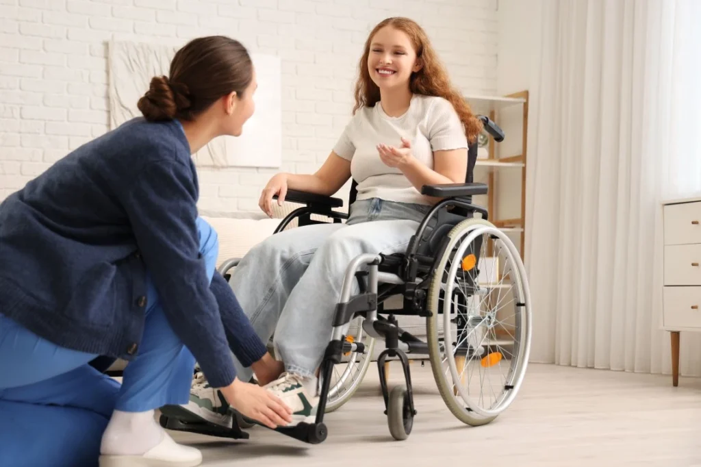 Disabled woman in wheelchair smiling at nurse in living room