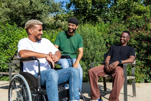 Disabled man in wheelchair laughing outside with two friends